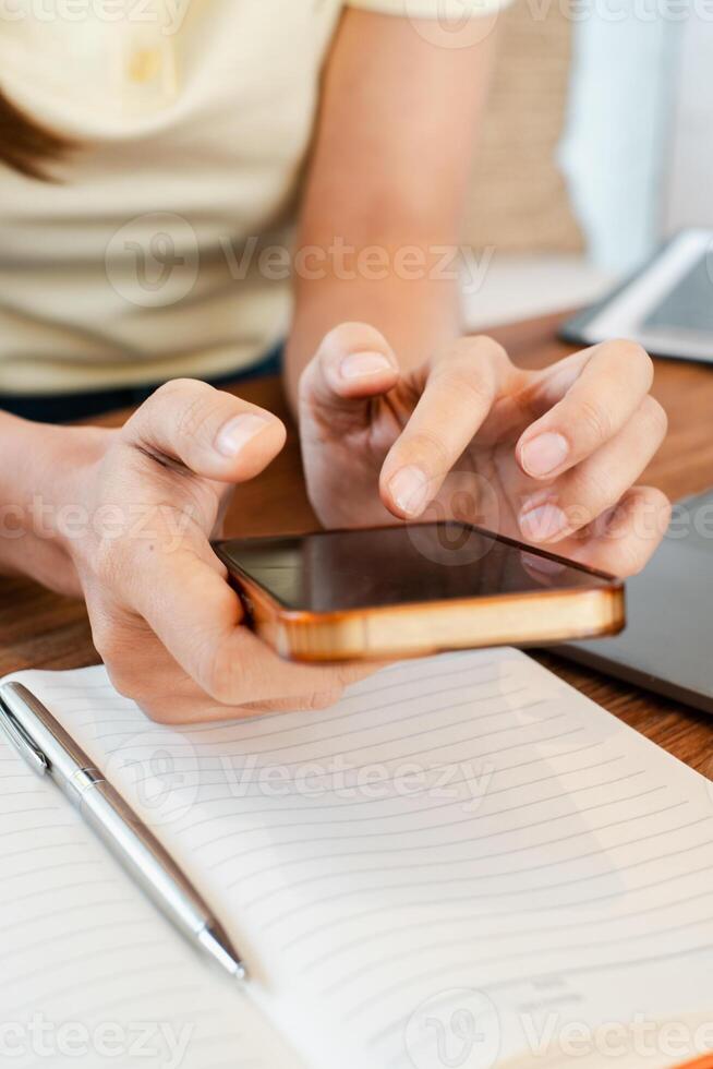 Hands holding a smartphone over a notebook with a pen on a wooden desk, capturing a moment of modern work or study. photo