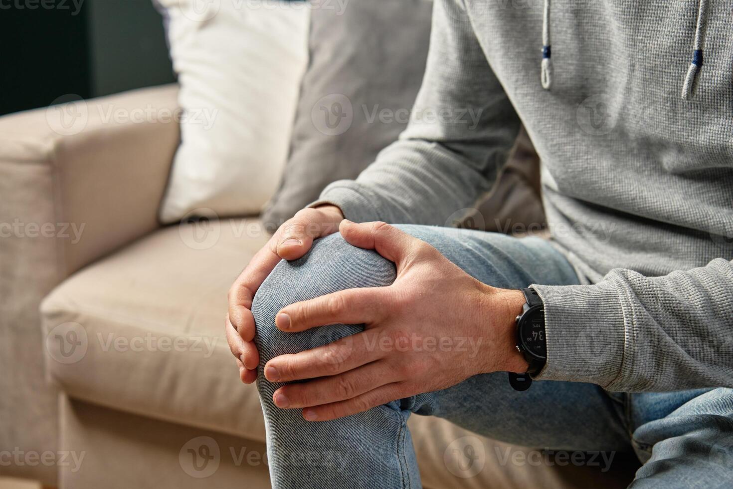 Man holding knee in pain while sitting on sofa photo
