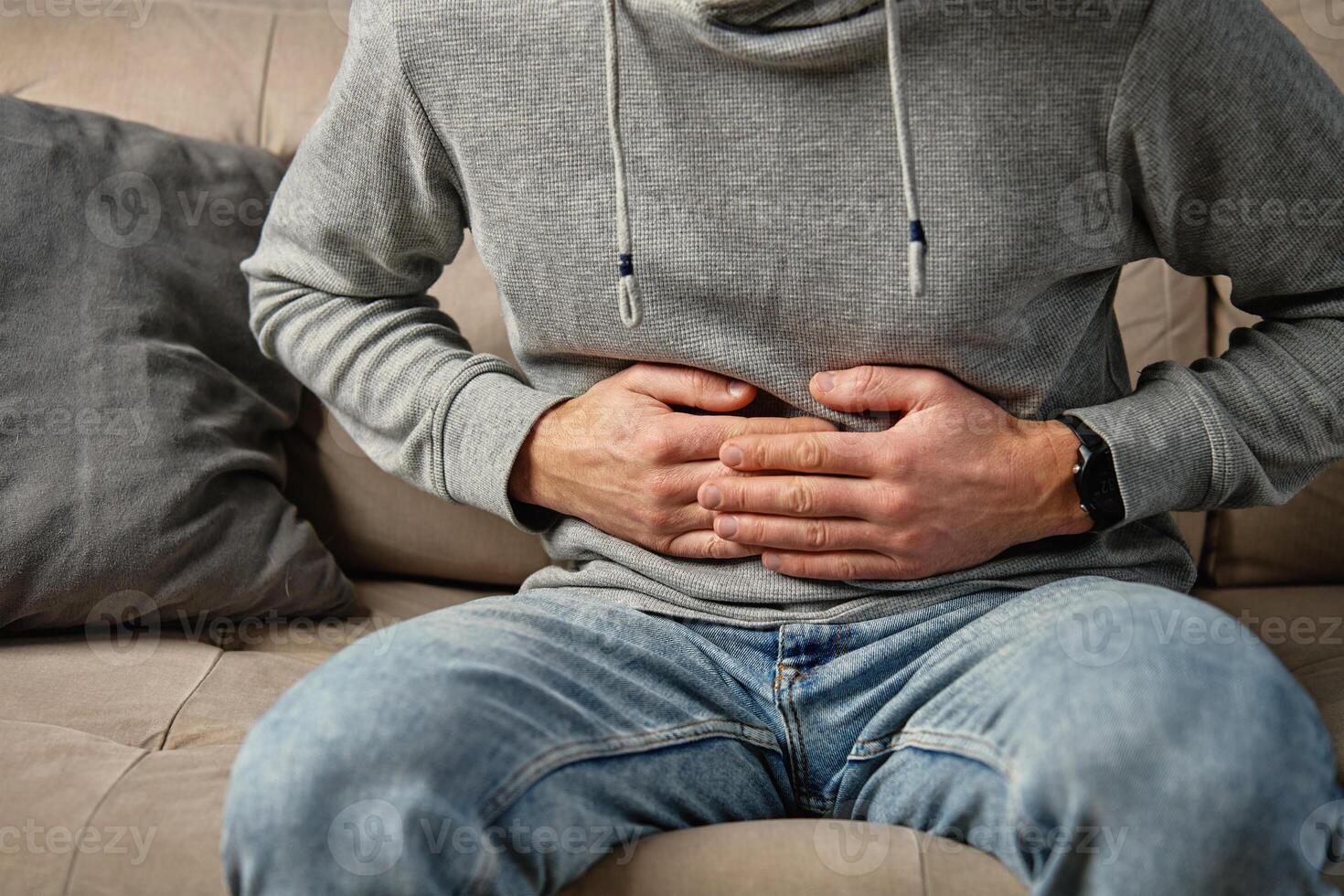 Man clutching stomach in pain. Person suffering from digestion problems at home photo
