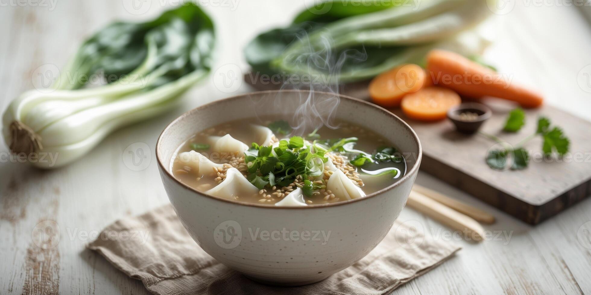 Steaming wonton soup served with fresh ingredients on a wooden table. photo