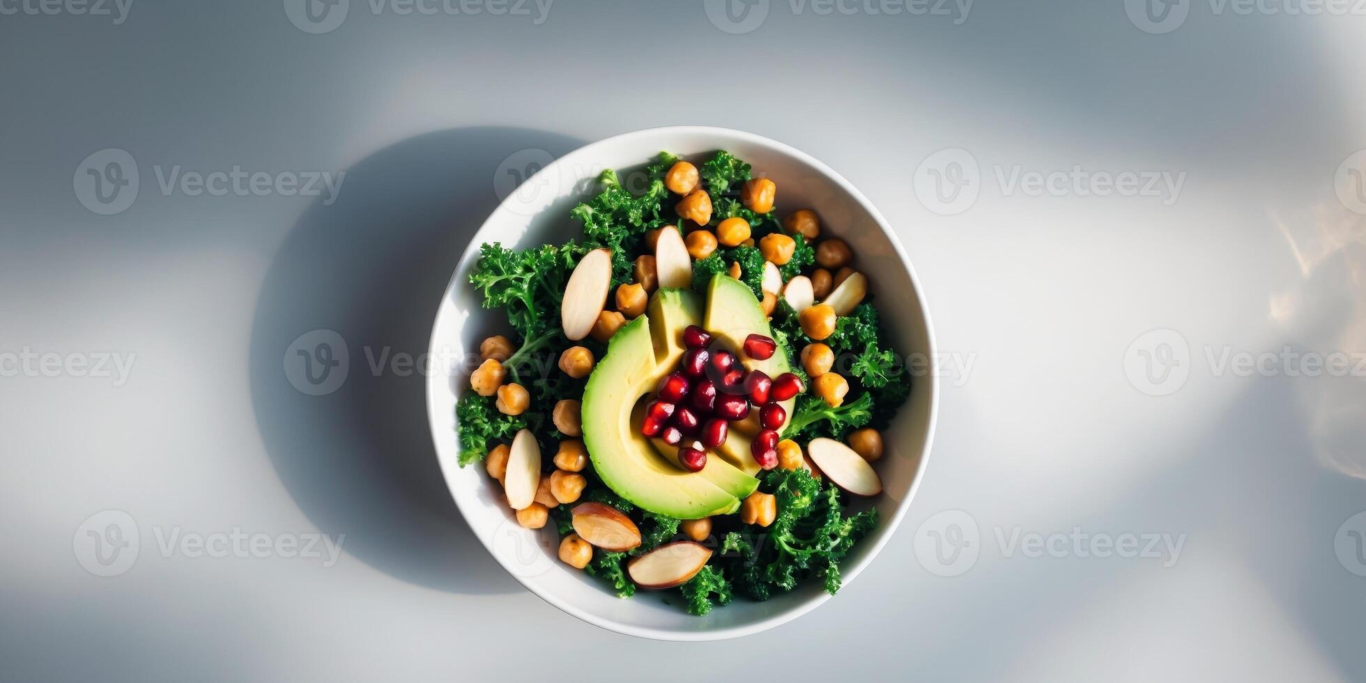 Avocado kale roasted chickpeas almond and pomegranate salad in white bowl healthy vegan food top view grey background. photo