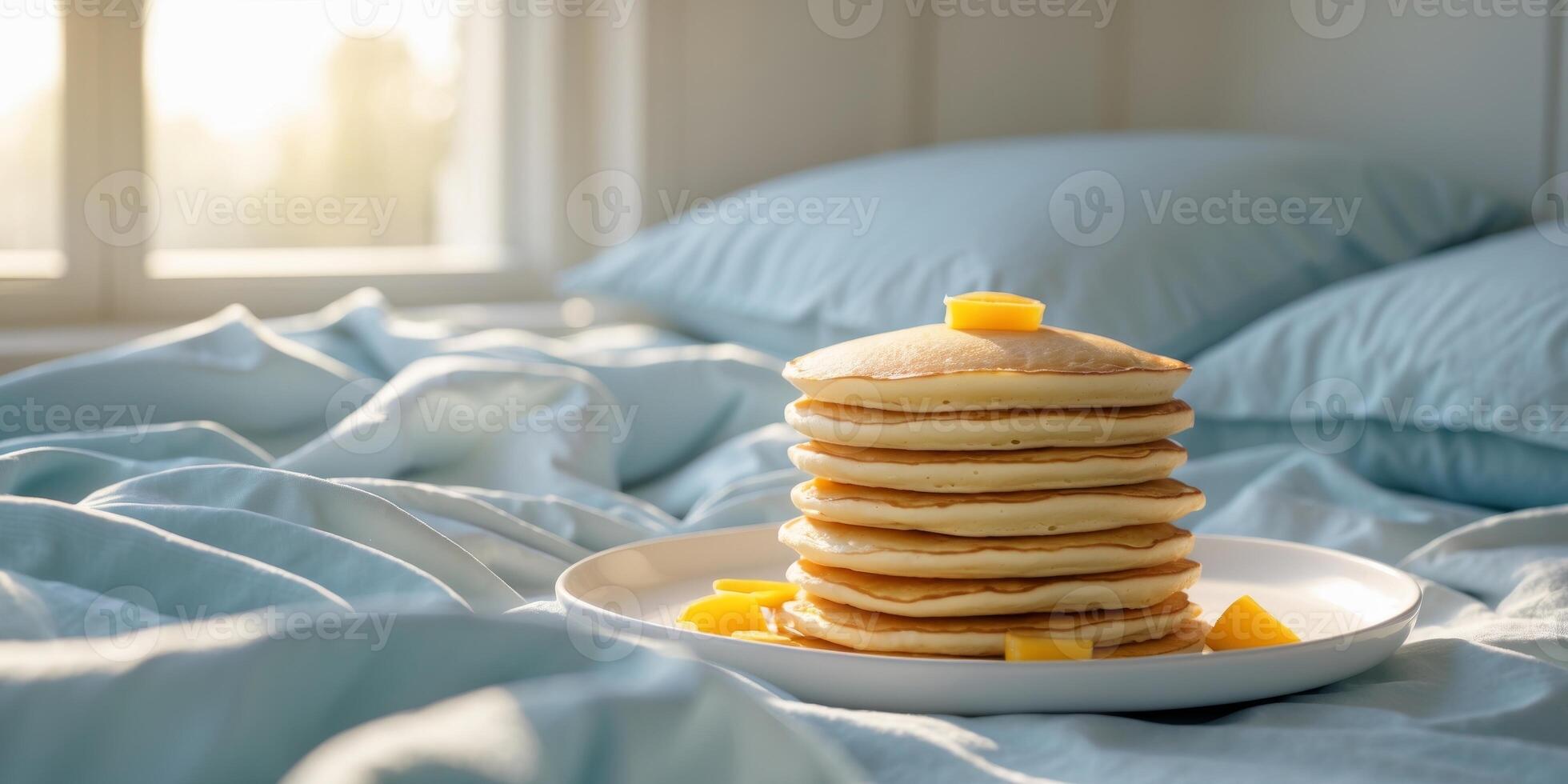 Stack of fluffy pancakes on a bed with light blue bedding and natural sunlight coming through a window with copy space photo