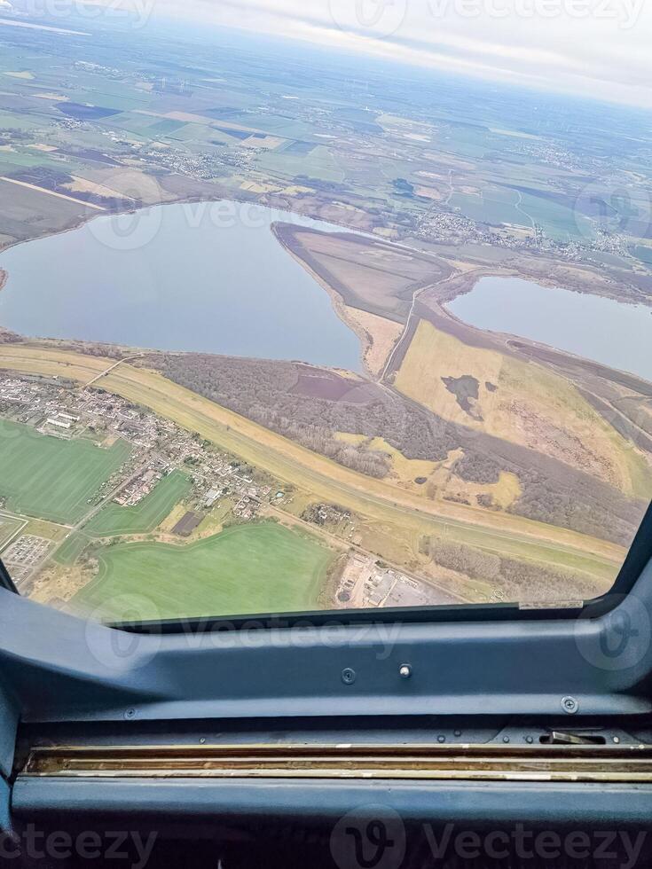 Aerial view from plane window. patchwork fields, lake, and small town under sky. High quality photo
