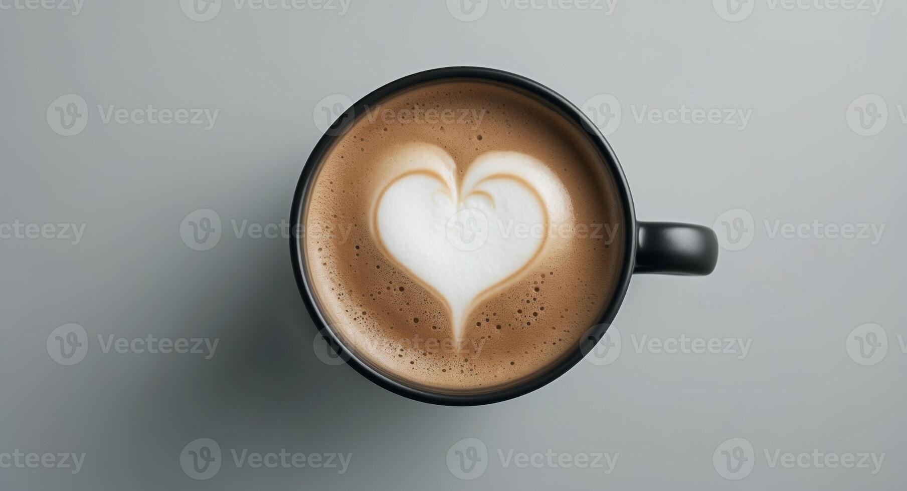 close up of black cup of cappuccino coffee on neat back background from above - foam forming a heart photo