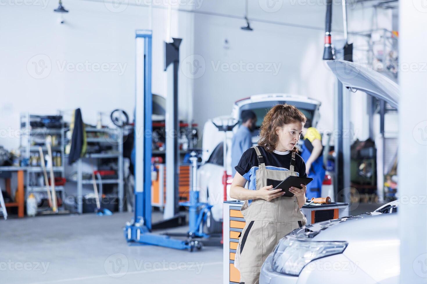Technician in car service uses tablet to calculate invoice for client after repairing radiator. Trained expert in garage calculating final costs after servicing customer vehicle photo