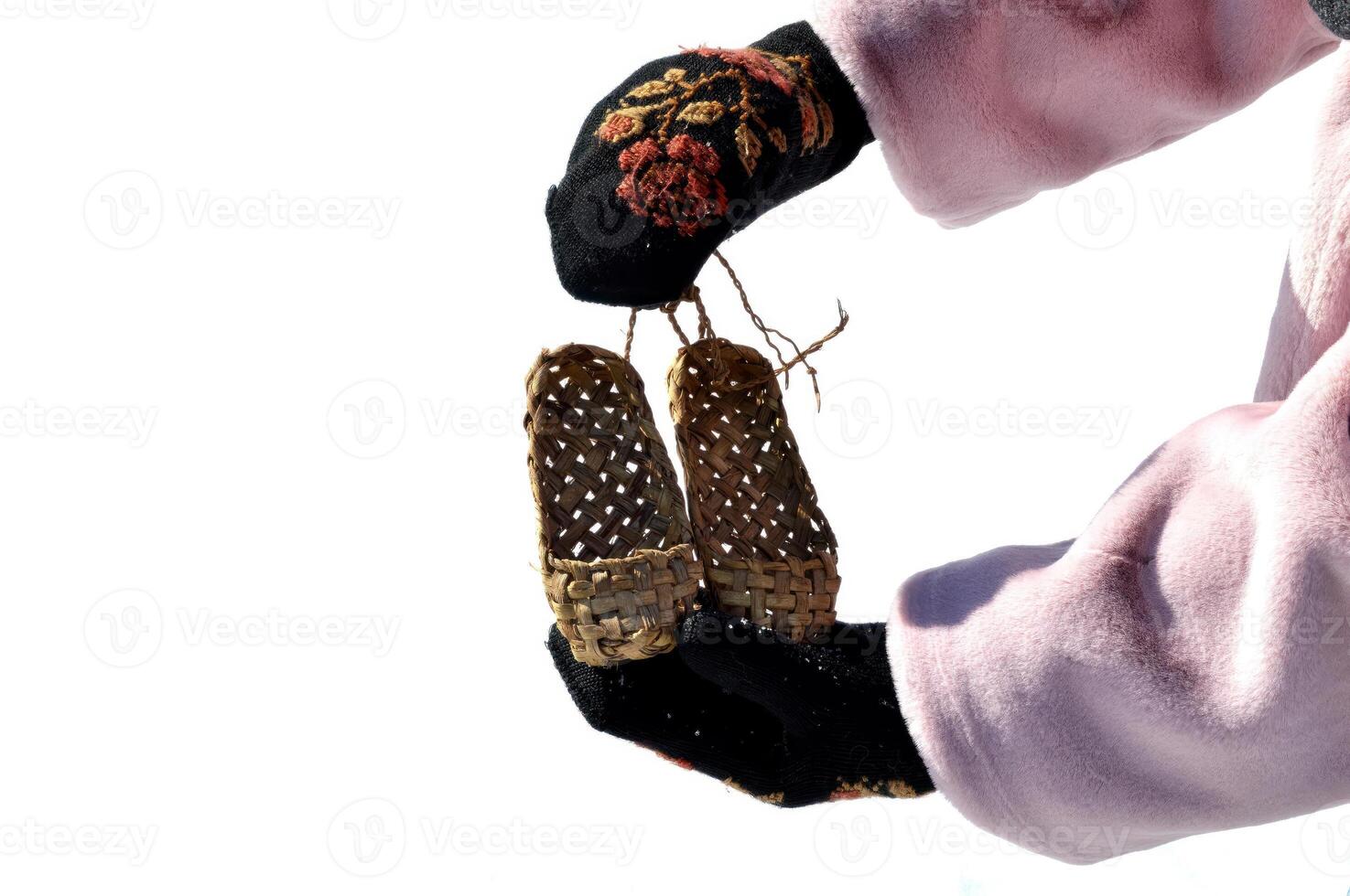 Hands with black mittens with russian traditional pattern holding bast shoes isolated on white background photo