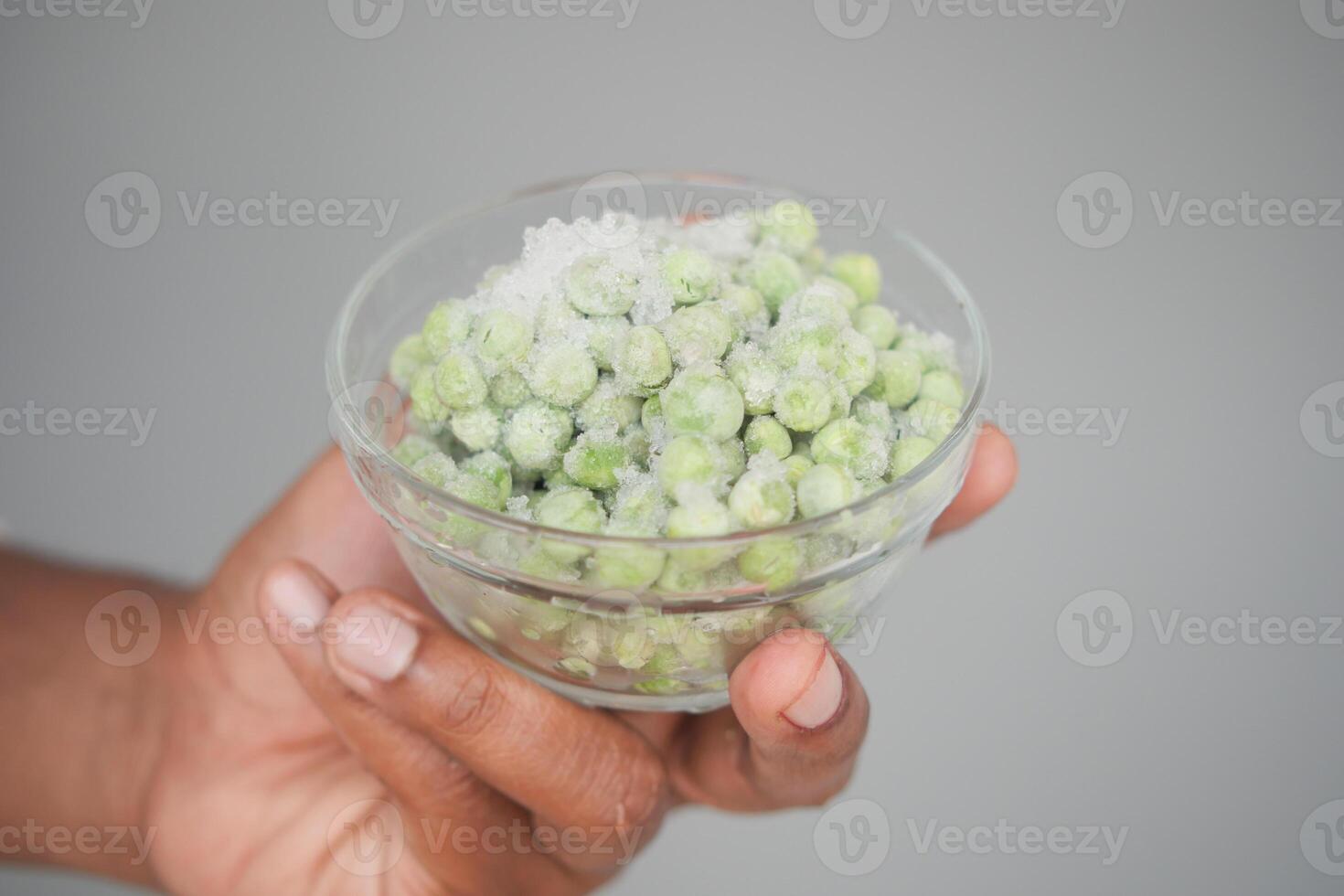 Bowl of frozen green peas held against a neutral background photo