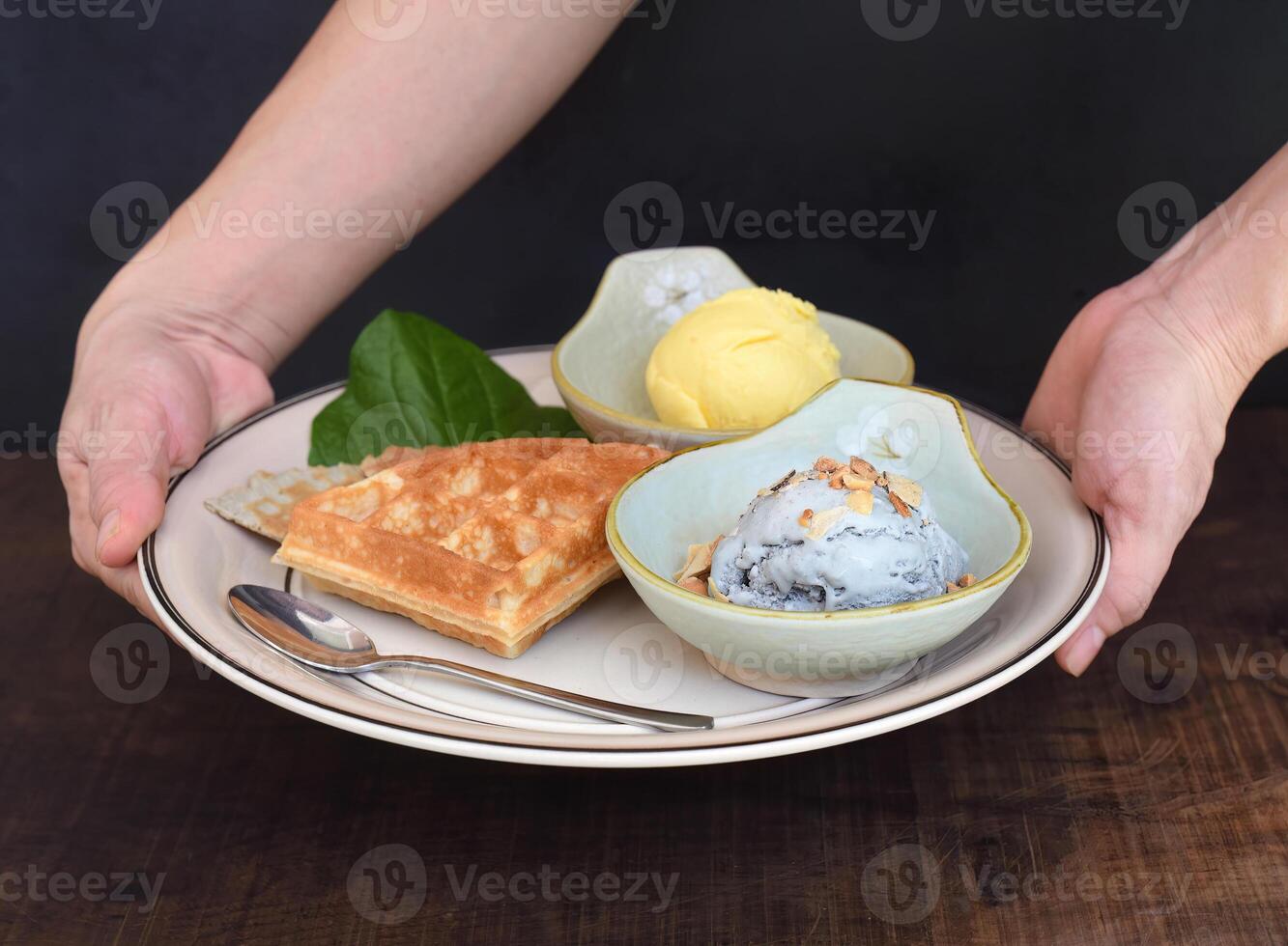 Hands hold dish with organic ice cream and Belgium waffles on wooden table background photo