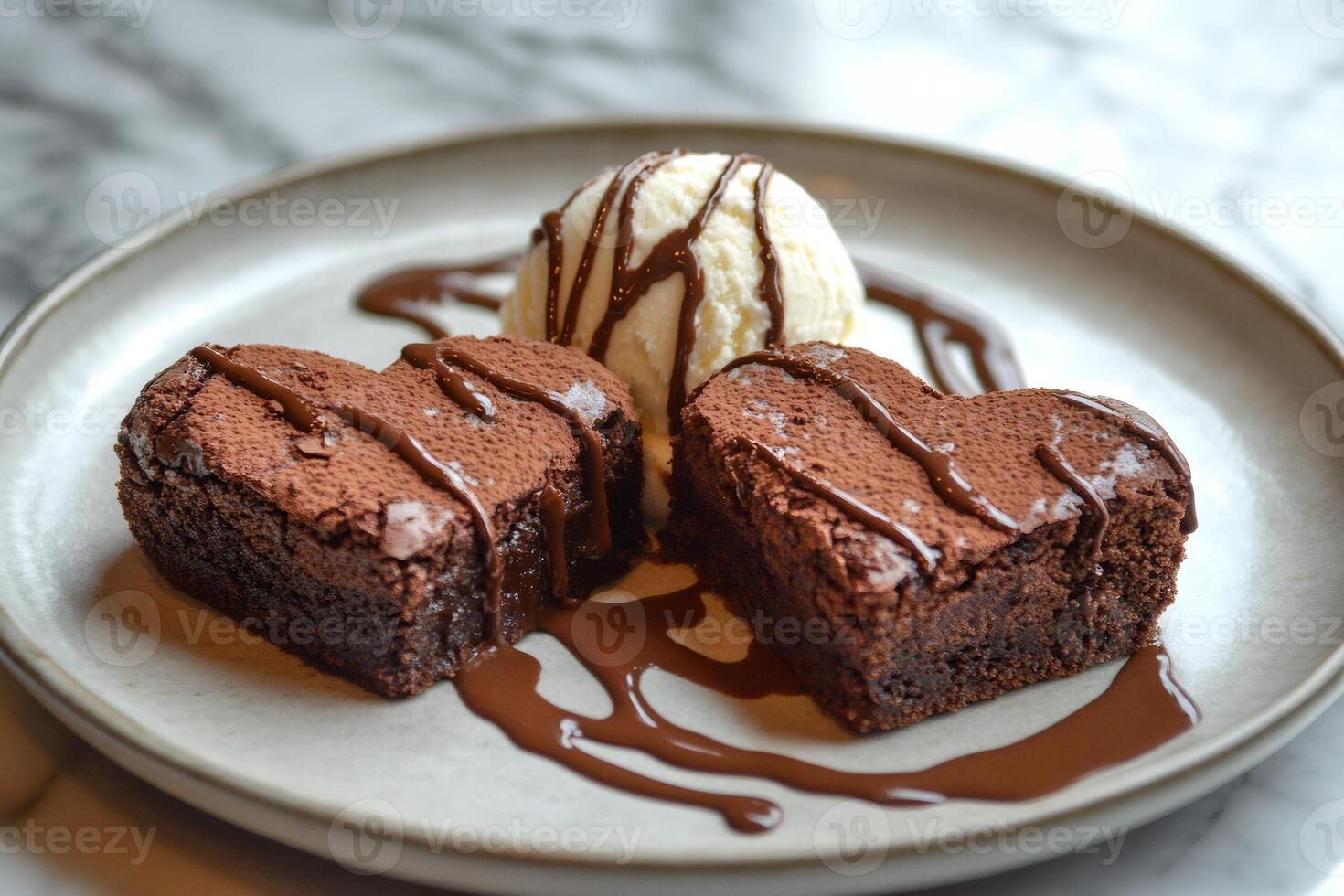 Two heart shaped brownies with vanilla ice cream and chocolate sauce are laying on a plate photo