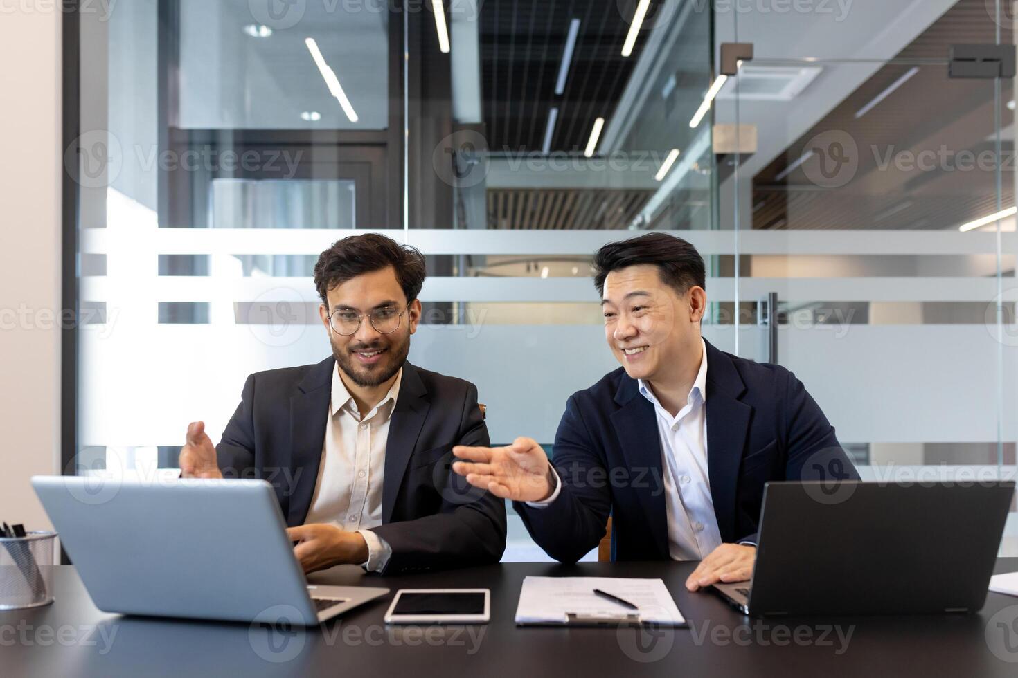 Business meeting, two men sitting inside office with laptops, smiling cheerfully discussing work project, team of people at workplace inside office. photo