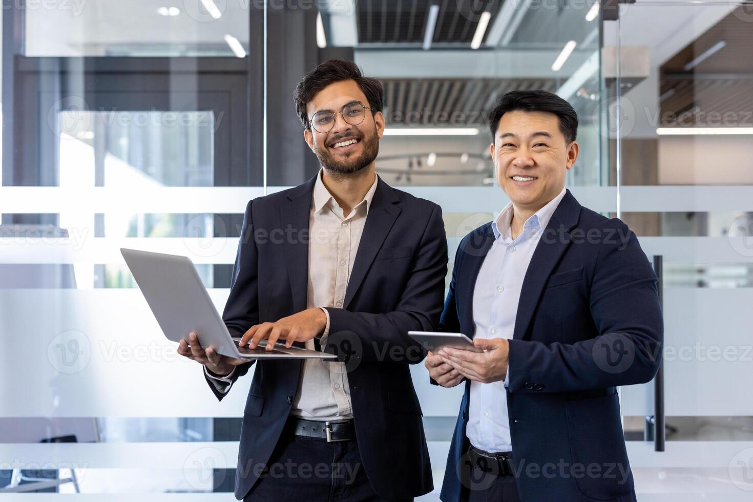 Two confident professionals engage in business discussion using laptop and phone in modern office. Smiling colleagues demonstrate teamwork, collaboration, and effective communication photo