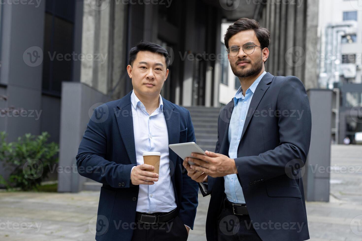 Two professional men in formal attire are engaged in a conversation outdoors in a cityscape. They appear to be collaborating or sharing ideas photo