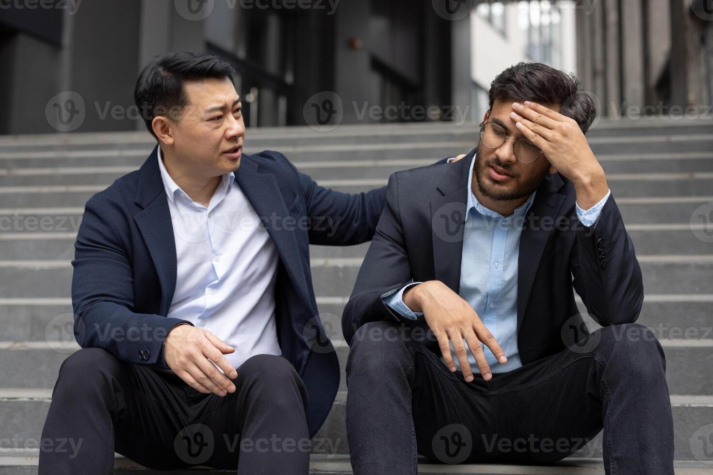 Business professional offering support to stressed colleague. Two men sit on office steps, one providing empathy and understanding during challenging work situation. Concept of support. photo