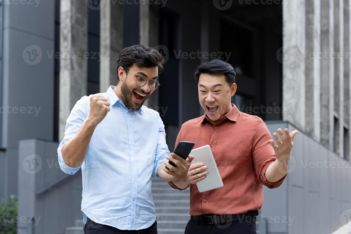 Two joyful colleagues cheerfully react to good news using a smartphone outdoors. Their jubilant expressions convey teamwork, achievement, and happiness in a professional setting photo