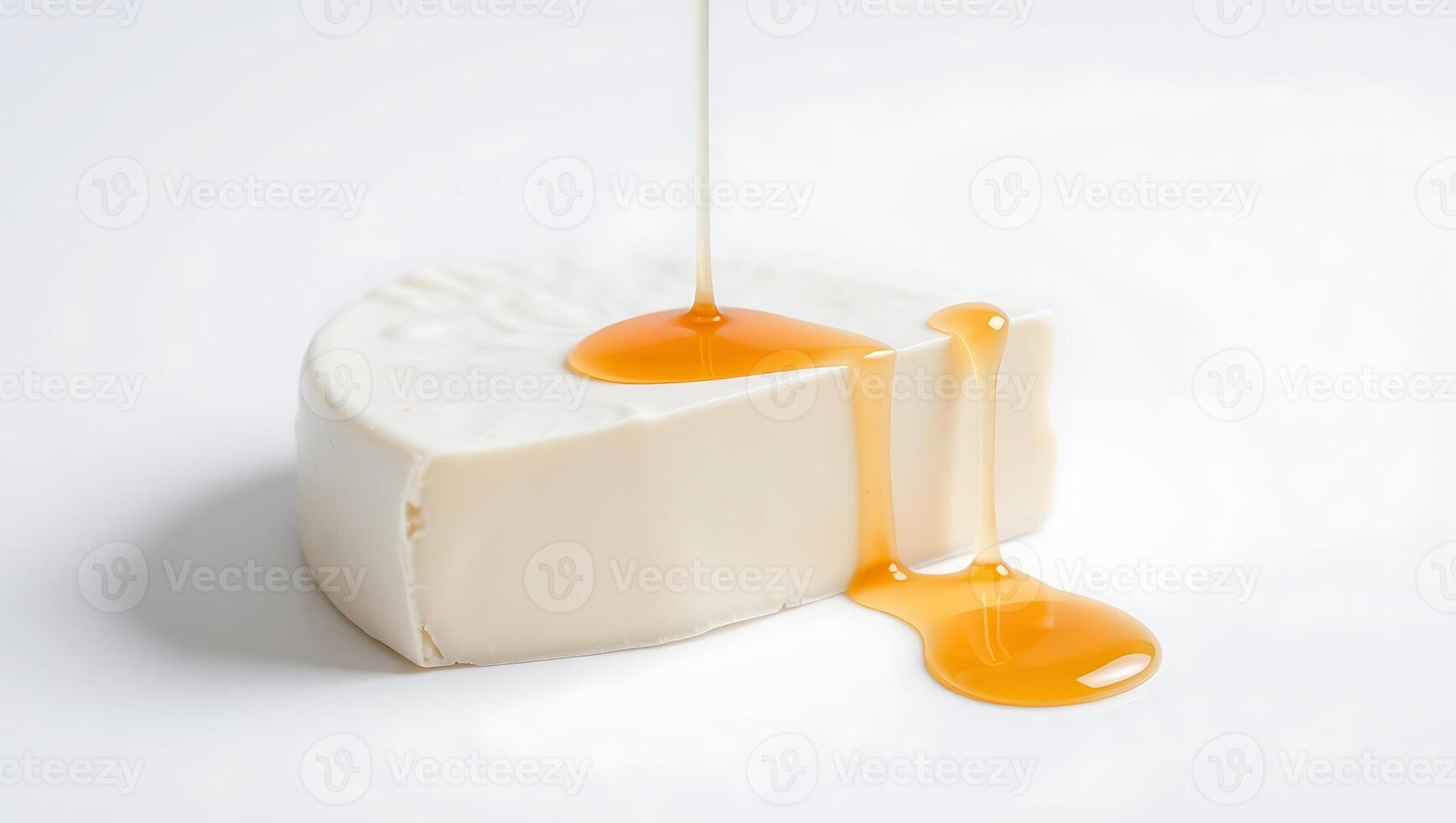 Honey pouring over a piece of soft cheese on a plain surface photo