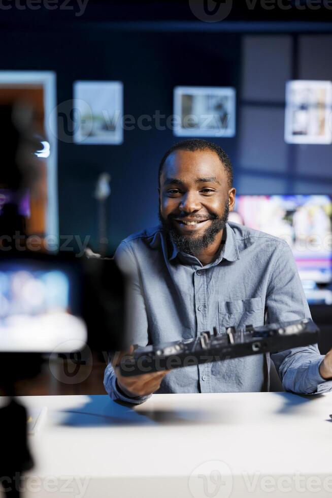 Cheerful BIPOC artist filming DJ mixing tutorial in recording studio, playing with samples and sound effects. Audio engineer showcasing music production equipment to audience photo