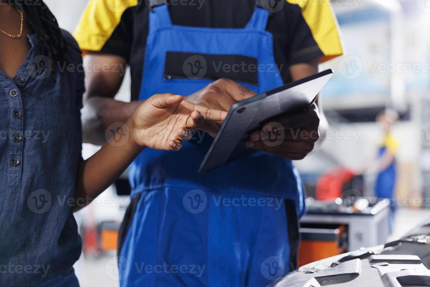 Mechanic in car service uses laptop to calculate invoice for client after repairing brakes. BIPOC employee in garage with customer calculating final costs after servicing vehicle, close up photo