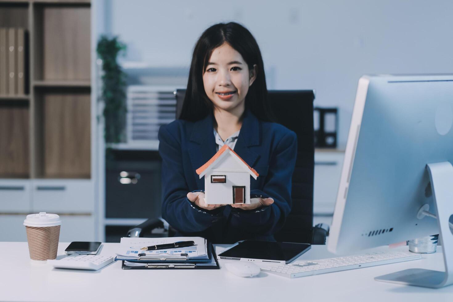 A woman in a business suit holding a house model photo