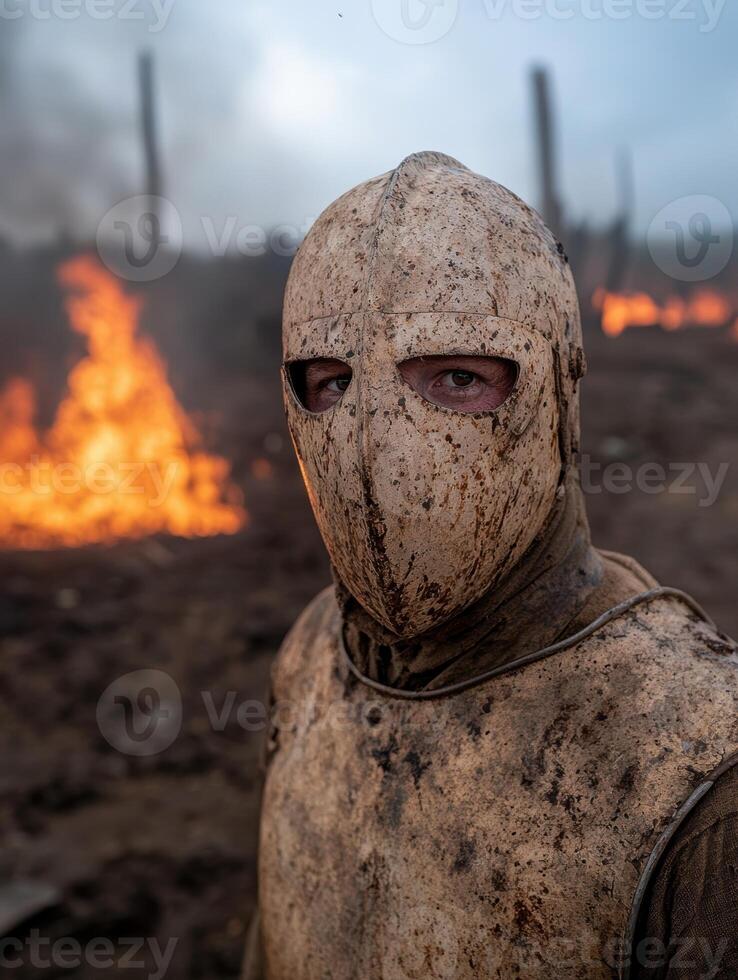 Medieval warrior in dirty armor and helmet near a fire photo