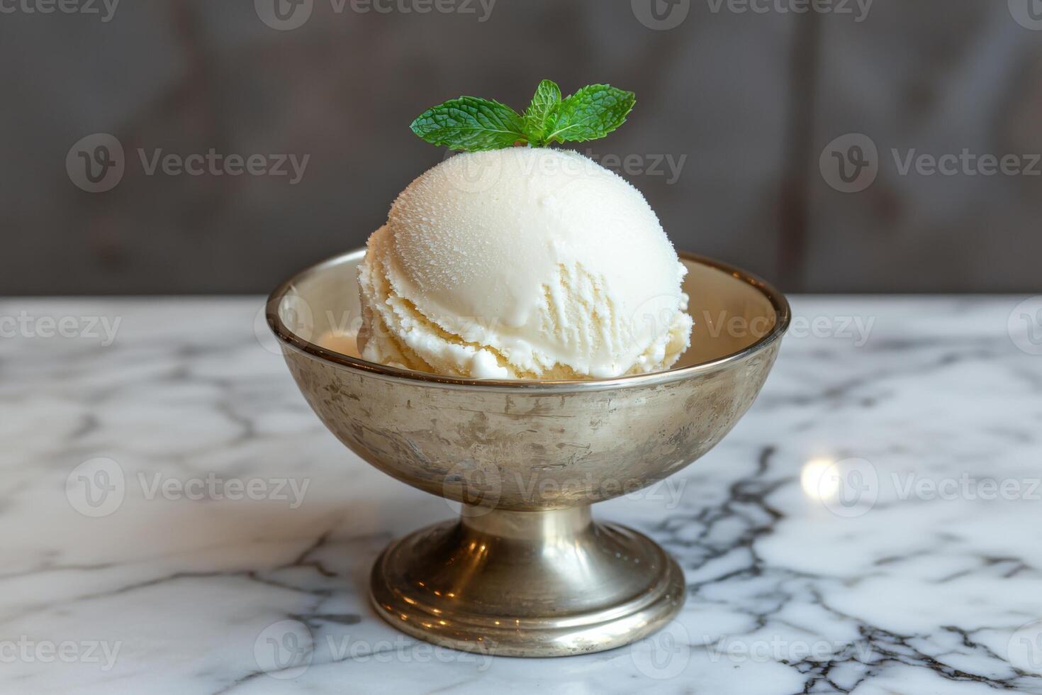 A scoop of vanilla ice cream in a silver bowl topped with mint photo