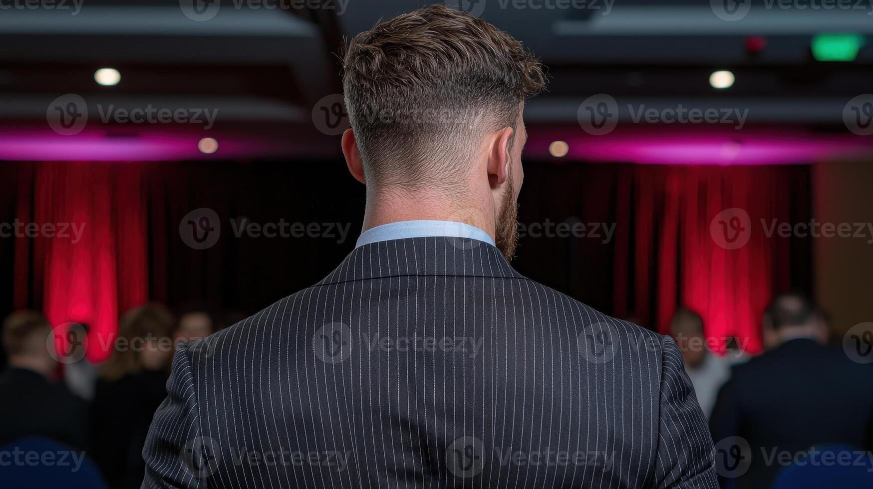 A man in a suit stands before an audience at a conference photo