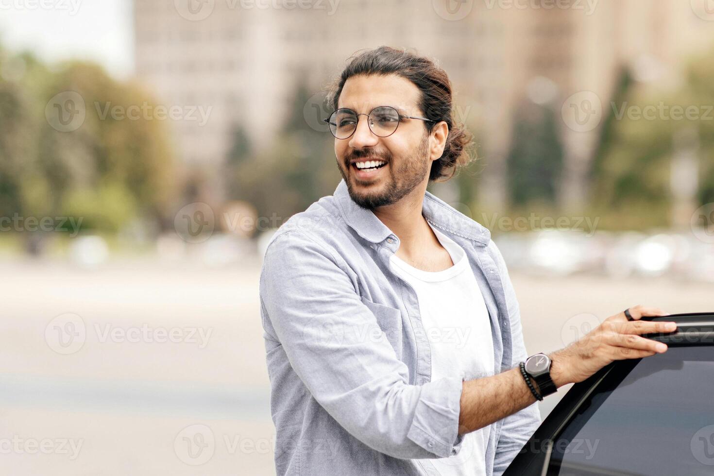 Stylish handsome middle-eastern man getting in white car, open auto back door, riding taxi home or to business meeting, looking at copy space. Car service, transportation concept photo