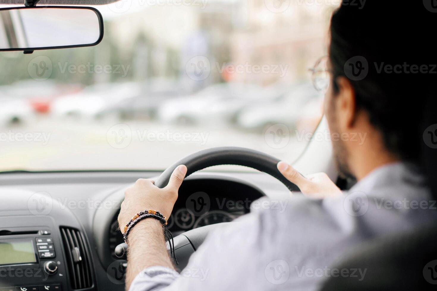 Rear view of indian long-haired man experienced driver driving auto, looking at road, copy space, shot from automobile back seat, closeup. Unrecognizable arab man enjoying his brand new car photo