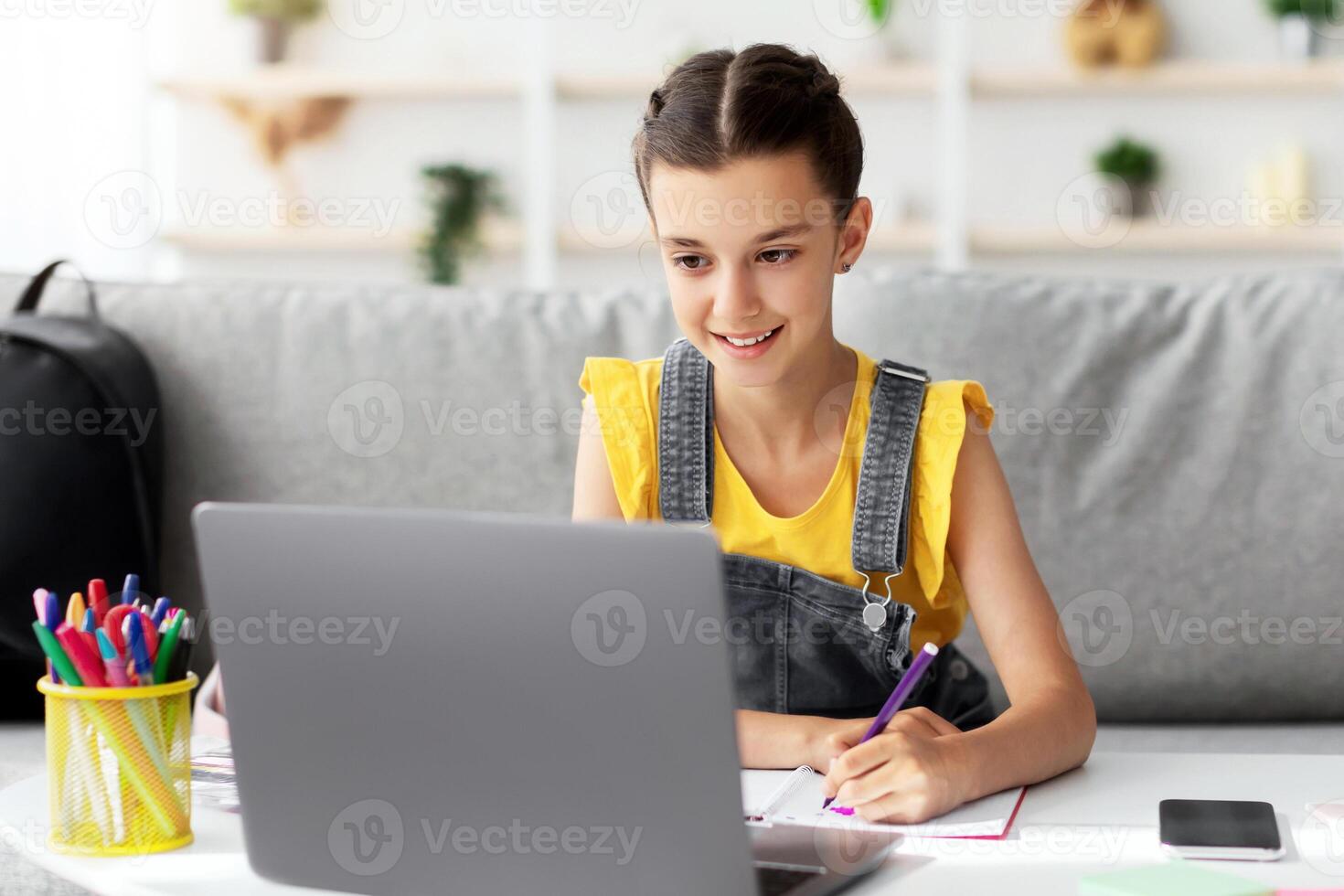 Portrait of smiling little girl drawing at home, using pc, happy schoolgirl looking at computer screen have fun in living room painting picture, studying online, holding marker photo