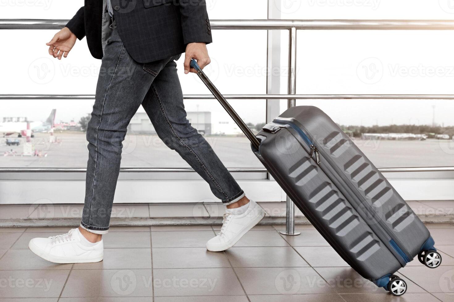 Air Transportation Concept. Unrecognizable man walking with suitcase in airport building, side view of male traveler carrying luggage, going to departure gate in terminal, cropped image, free space photo