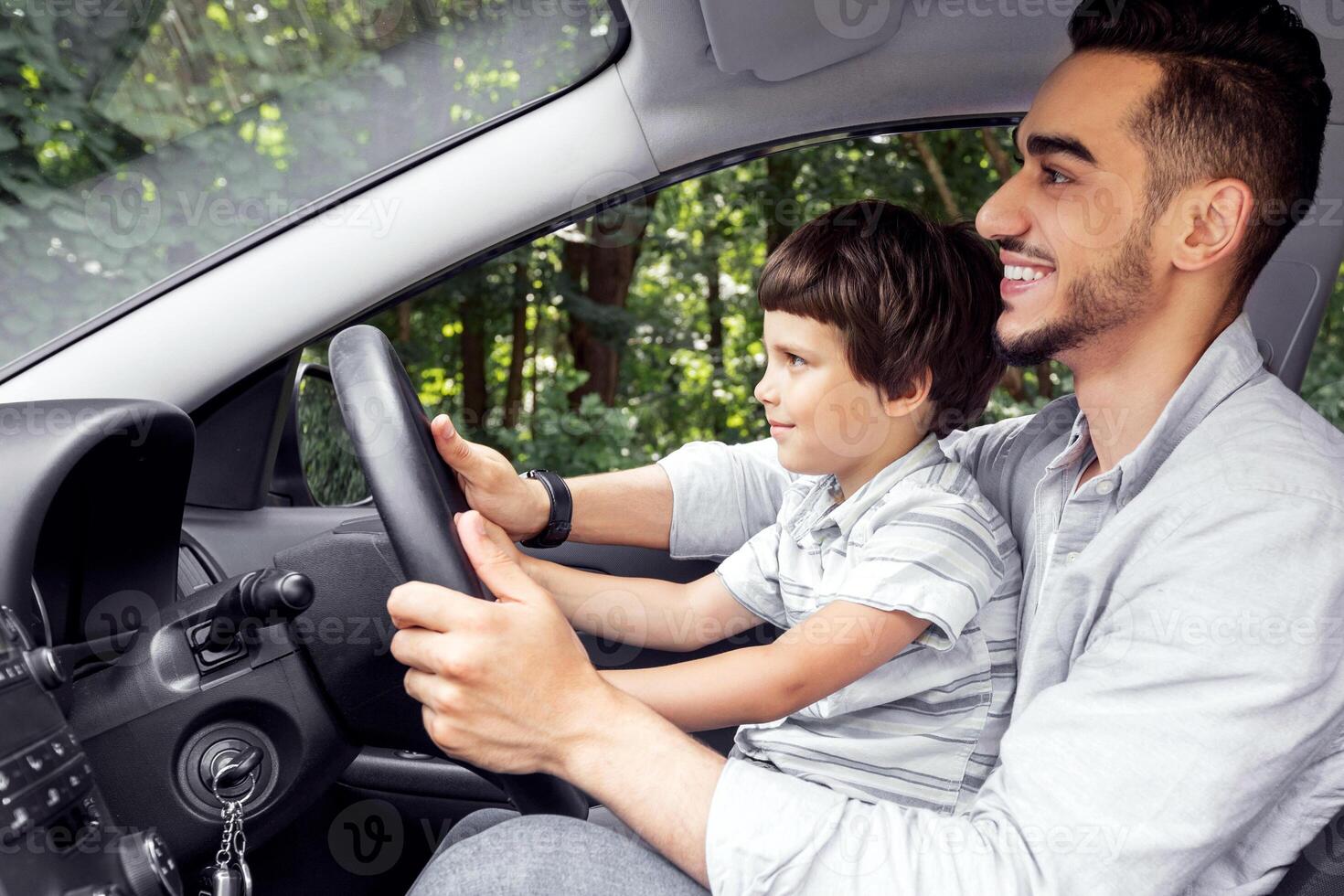 Happy millennial dad teaching little boy with steering wheel to drive car in summer, outdoor, profile. Family enjoy time together at weekend, road trip and driving lesson. Father and son at spare time photo