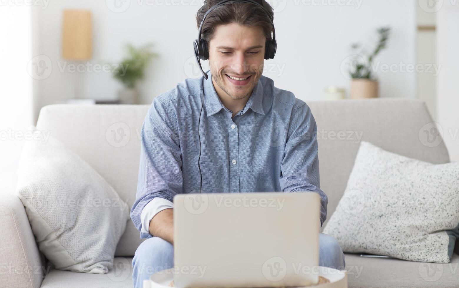Positive Man In Earphones Using Laptop Listening To Podcast Or Taking Part In Webinar Sitting On Sofa At Home. photo