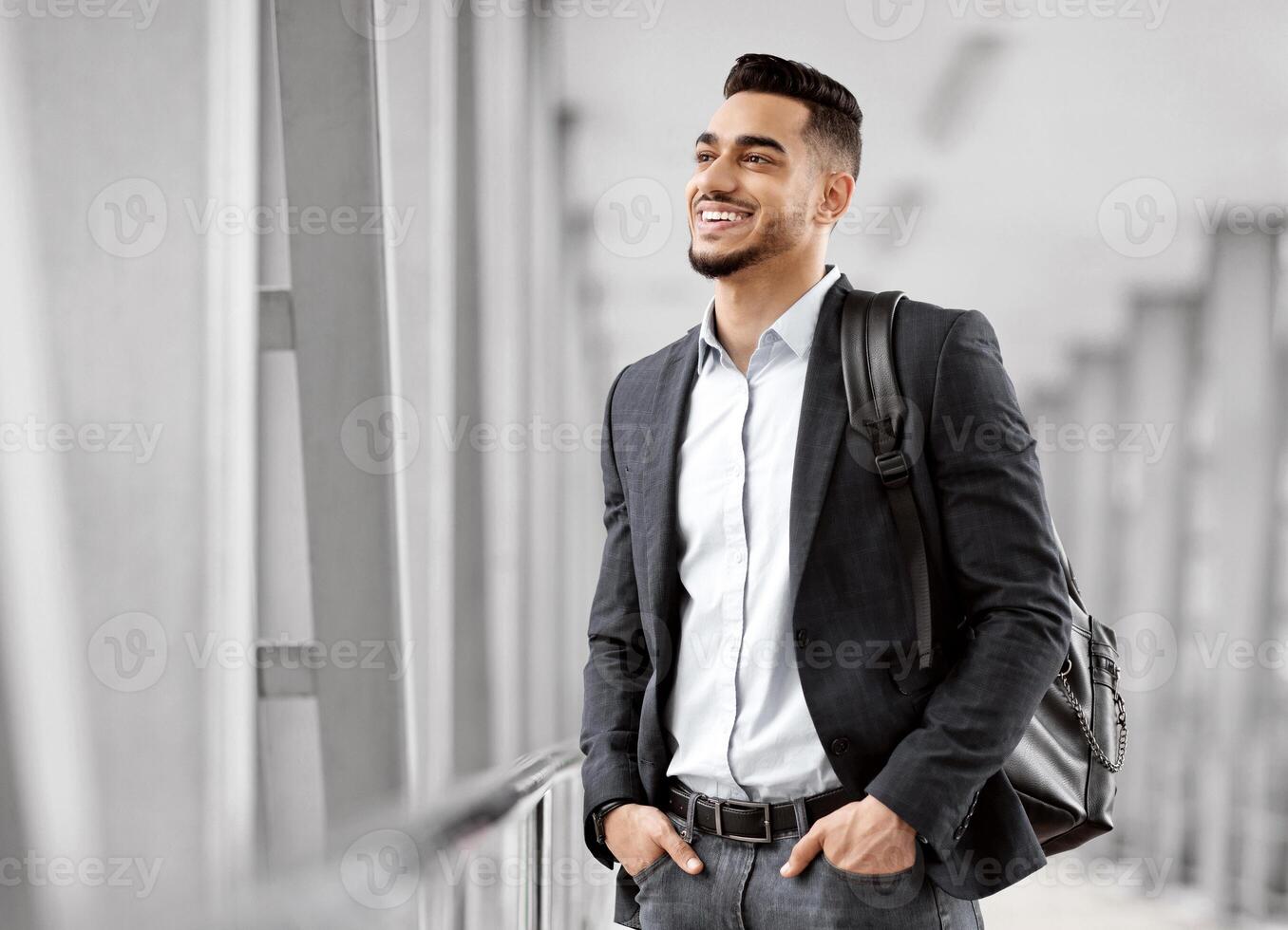 Ready For Trip. Handsome Arab Man With Backpack Standing At Airport Terminal And Looking At Window, Smiling Middle Eastern Man Waiting For Flight Departure, Enjoying Air Travels, Copy Space photo