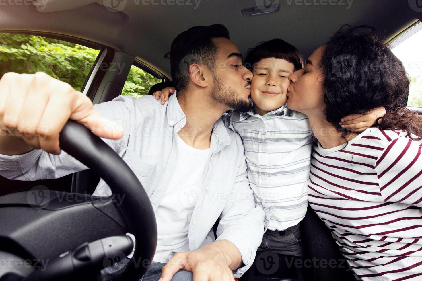 Family Trip. Happy Arab Parents Kissing Their Son While Riding Car Together, Loving Middle Eastern Mom And Dad And Their Male Child Enjoying Automobile Travels, Closeup Shot Inside Of Vehicle photo