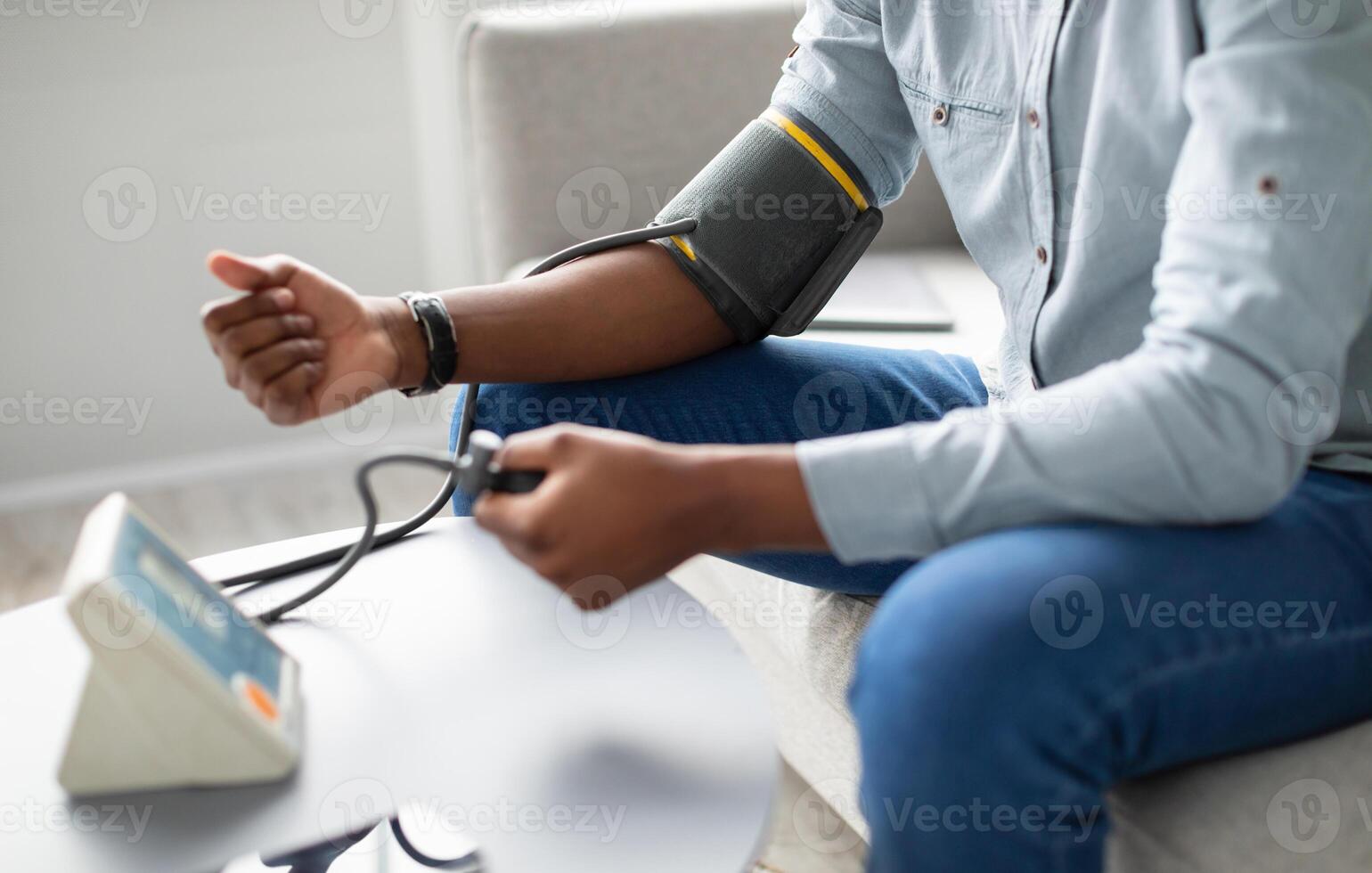 Unrecognizable African Guy Measuring Arterial Pressure Having Hypertension Sitting On Sofa At Home. Cropped. Health Problem With Low And High Blood Tension, Blood-Pressure Checkup. Selective Focus photo