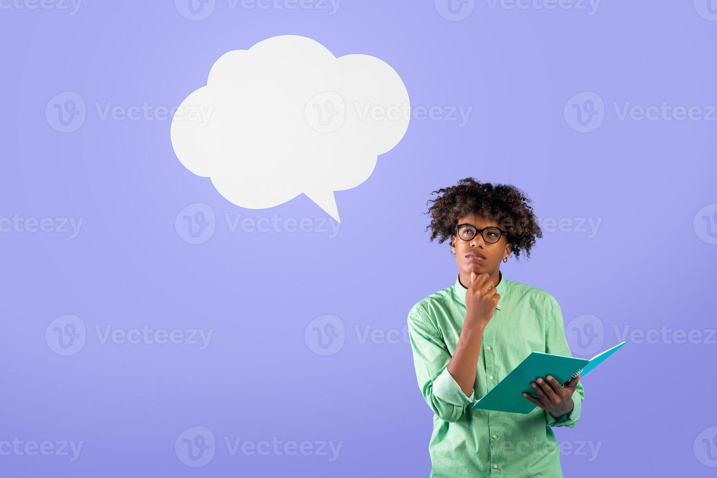 Think and make decisions. Pensive black guy in glasses holding notebook and toching chin, looking up at empty space, isolated on blue background, studio shot photo