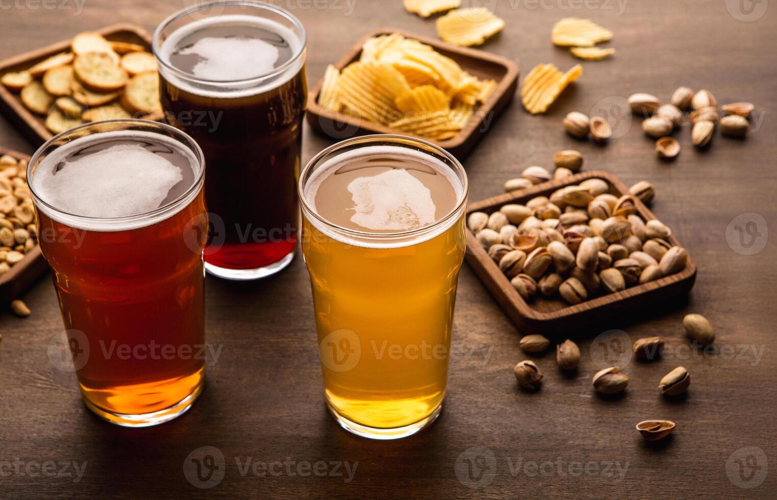 Table for company of friends. Crispy snacks and different types of beer in glasses on wooden background, close up photo
