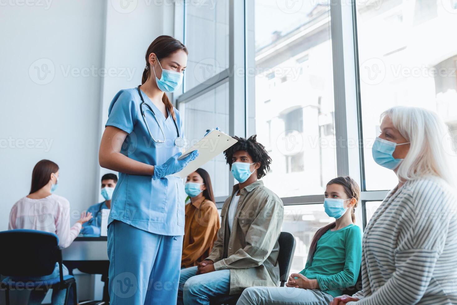 Coronavirus Vaccination. Diverse People Group Waiting For flu Vaccine Sitting In Queue In Hospital Waiting-Room, Nurse Registering Patients. Corona Virus Prevention, Medical Immunization Campaign photo