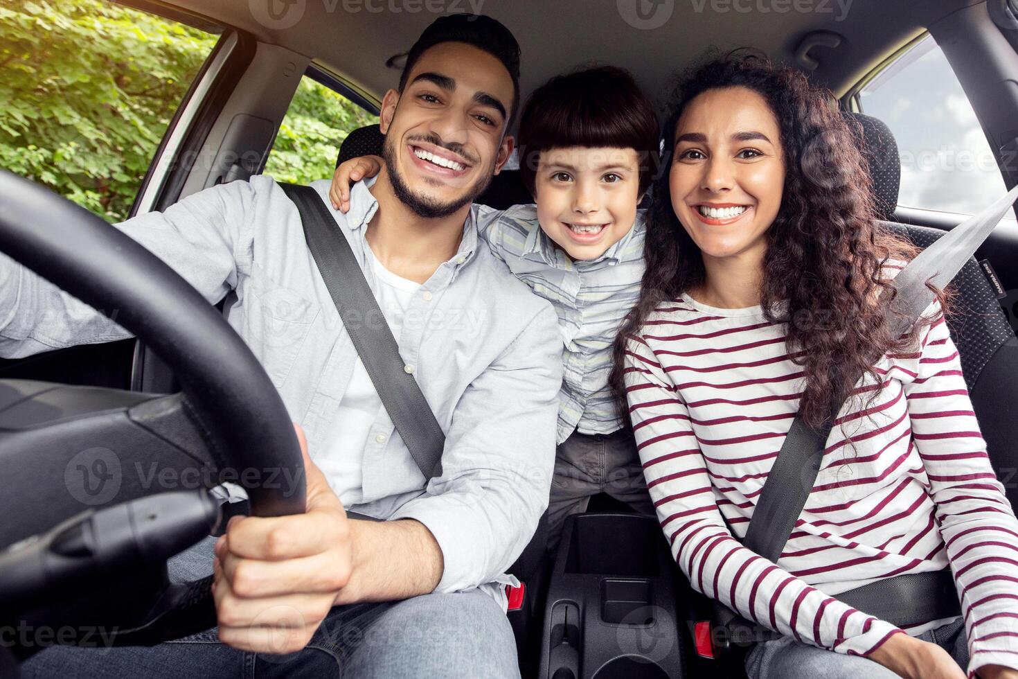 Happy Arab Family With Little Son Sitting Inside Of Car And Smiling At Camera, Cheerful Middle Eastern Parents With Cute Male Kid Enjoying Road Trip In Their New Automobile, Closeup Shot photo