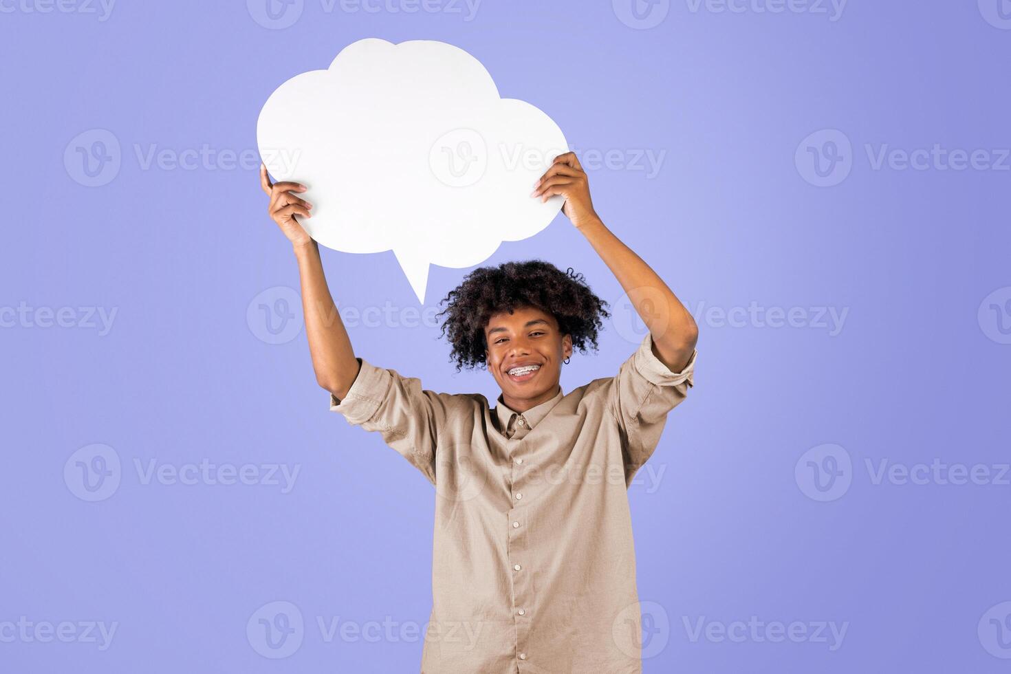 Positive african american teenager holding empty speech bubble above his head over blue background, mockup for your ad or design. Black guy with empty word cloud smiling to camera photo