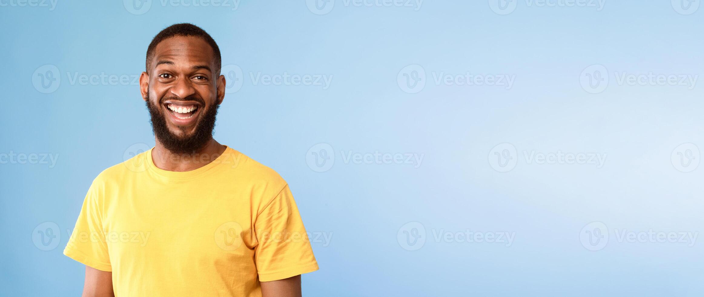 Positive young African American man in casual wear smiling and looking at camera on blue background, panorama with empty space. Handsome millennial guy having cheerful face expression photo