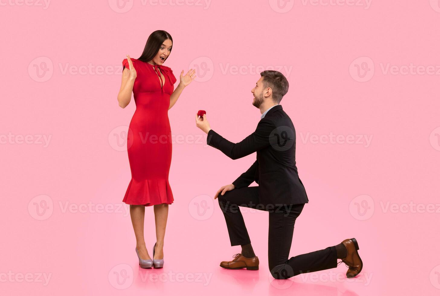 Proposal. Loving Man Offering Surprised Girlfriend Engagement Ring Standing On One Knee Over Yellow Studio Background photo