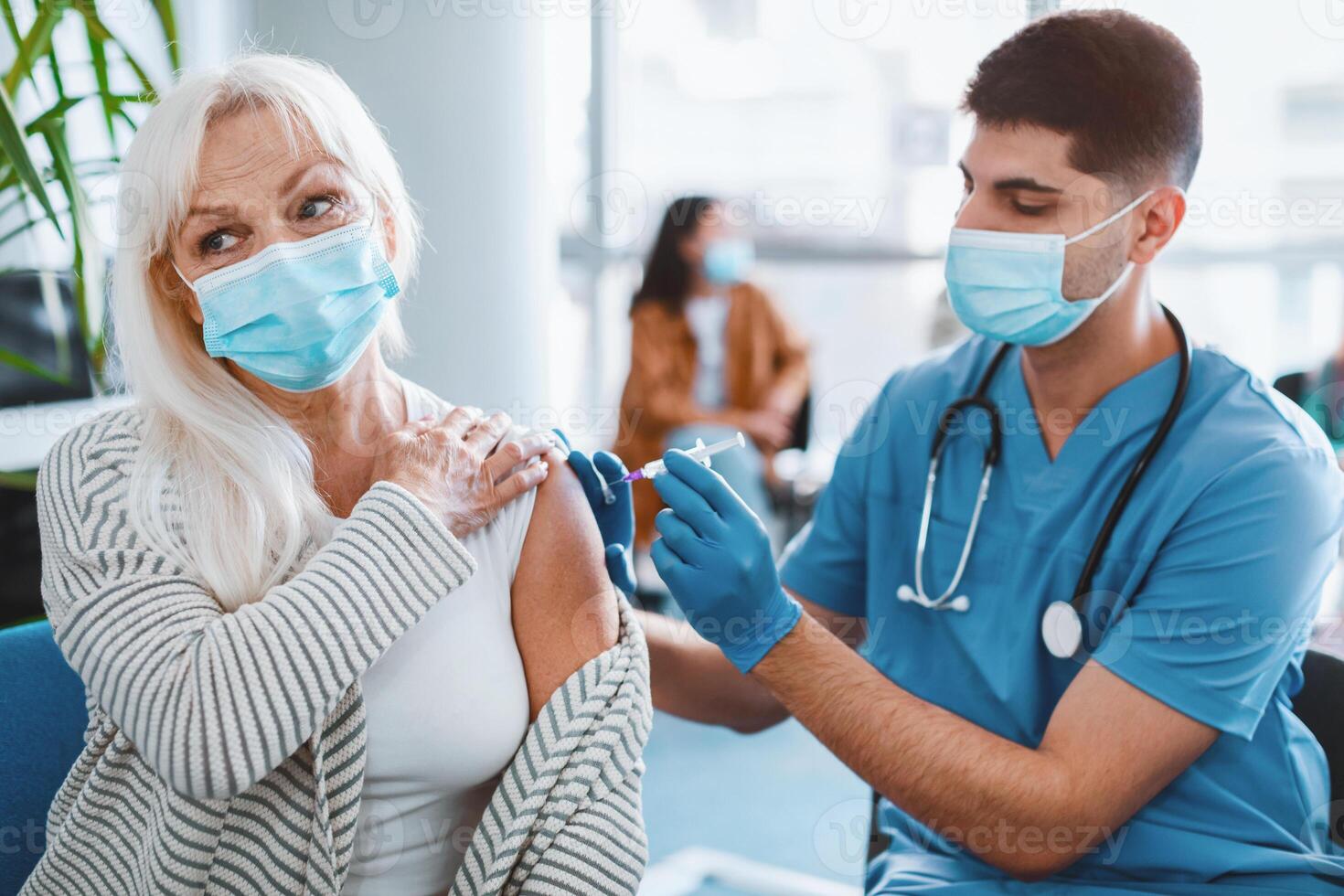 Nurse or doctor in medical face mask giving injection to older patient during mass immunization campaign at health center. Senior woman getting flu vaccine shot at clinic or hospital photo