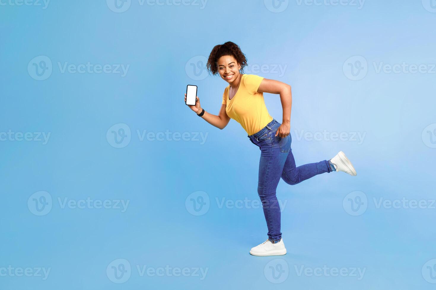 Huge online sale. Full length of happy young African American woman with blank smartphone running on blue studio background, mockup for website or mobile app. Space for cool advertisement template photo