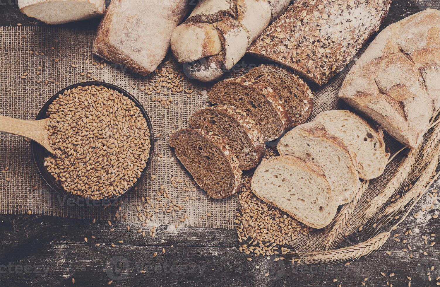 Plenty of sliced bread background. Bakery and grocery concept. Fresh, healthy whole grain sliced sorts of rye and white loaves, sprinkled flour on sackcloth and rustic wood table, food top view photo