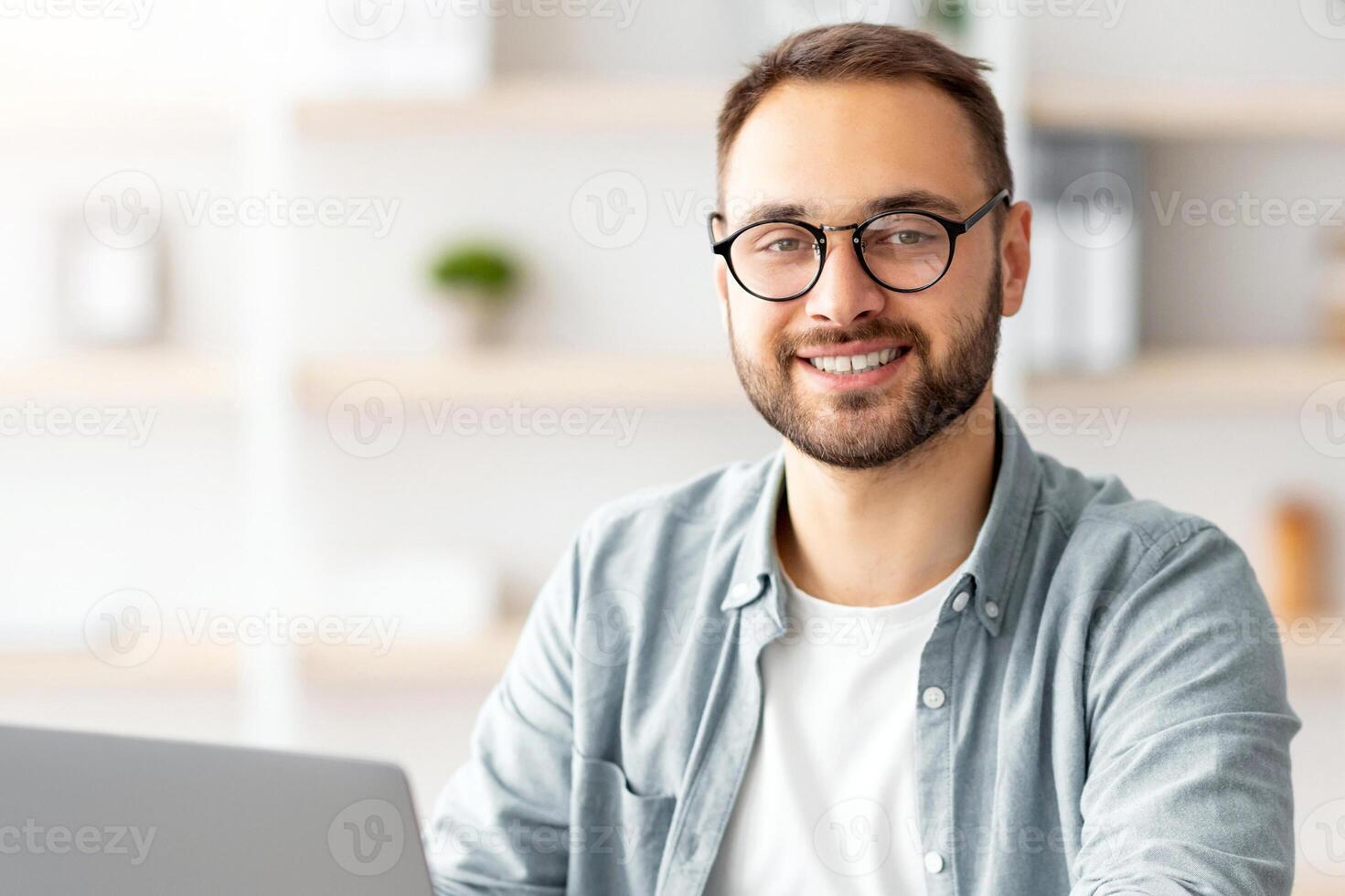 Happy young guy sitting at table with flag of Germany, using laptop pc, studying foreign language online at home. Modern remote education, abroad work and citizenship concept photo
