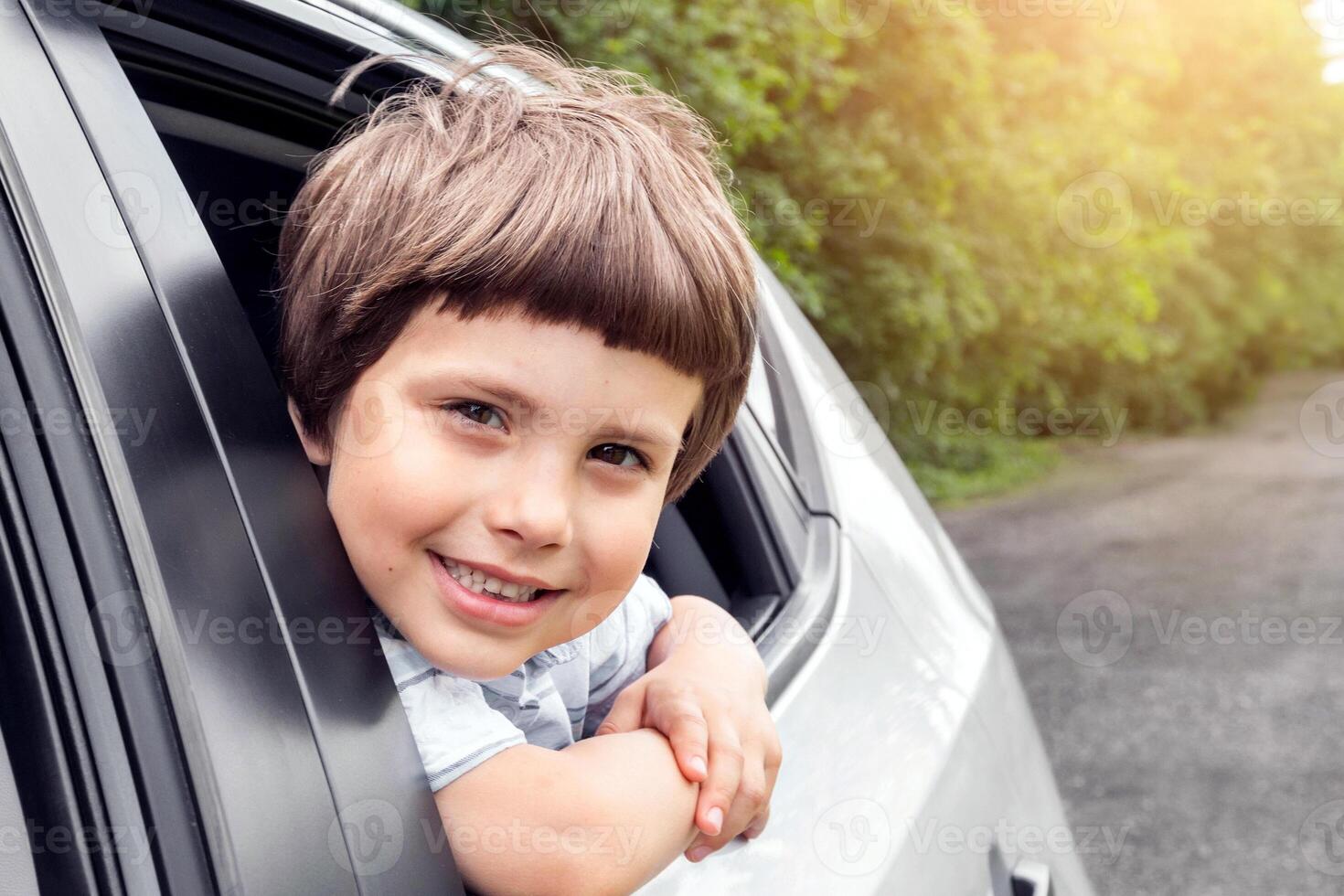 Smiling little boy rides in car, looks out the open window, have fun, enjoying auto ride, outdoors in summer, close up, free space. Weekend trip with family, road and vacation together, auto journey photo