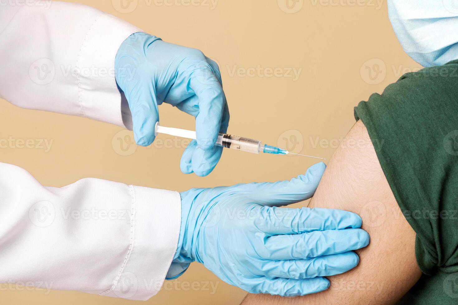 Nurse making intramuscualr injection against coronavirus for arab man at clinic, patient wearing protective face mask, closeup, doc with syringe vaccinating indian young guy while COVID-19 pandemic photo
