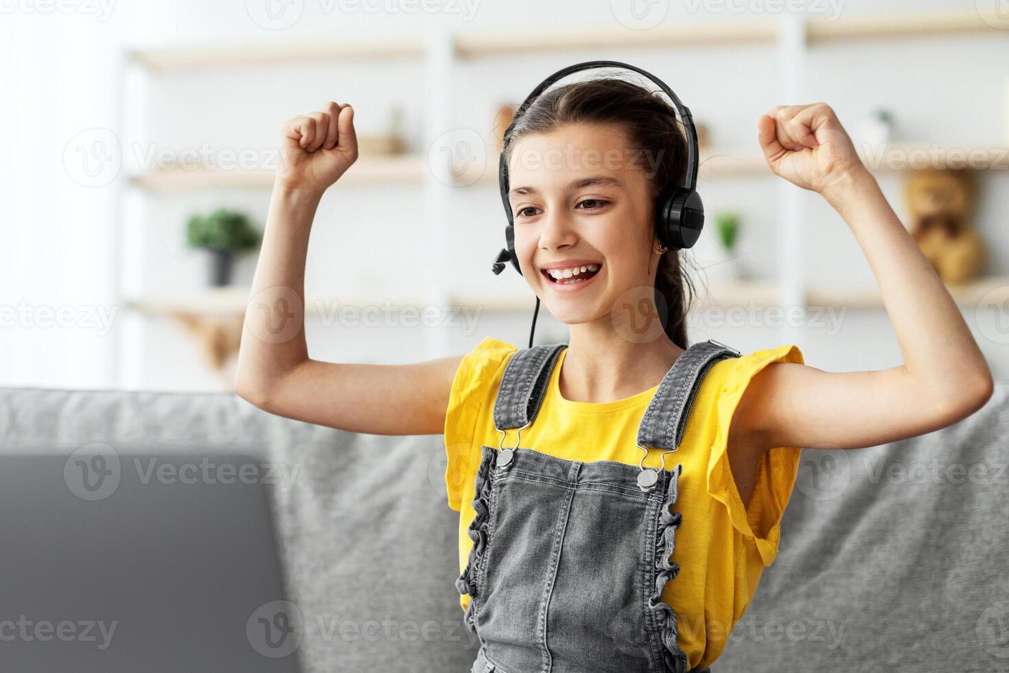 Joy Of Victory. Emotional Girl In Headset Shaking Clenched Fists Celebrating Success Sitting At Desk With Pc At Home. Yes, I Did It Concept. Positive Emotion And Expression, Free Copy Space photo