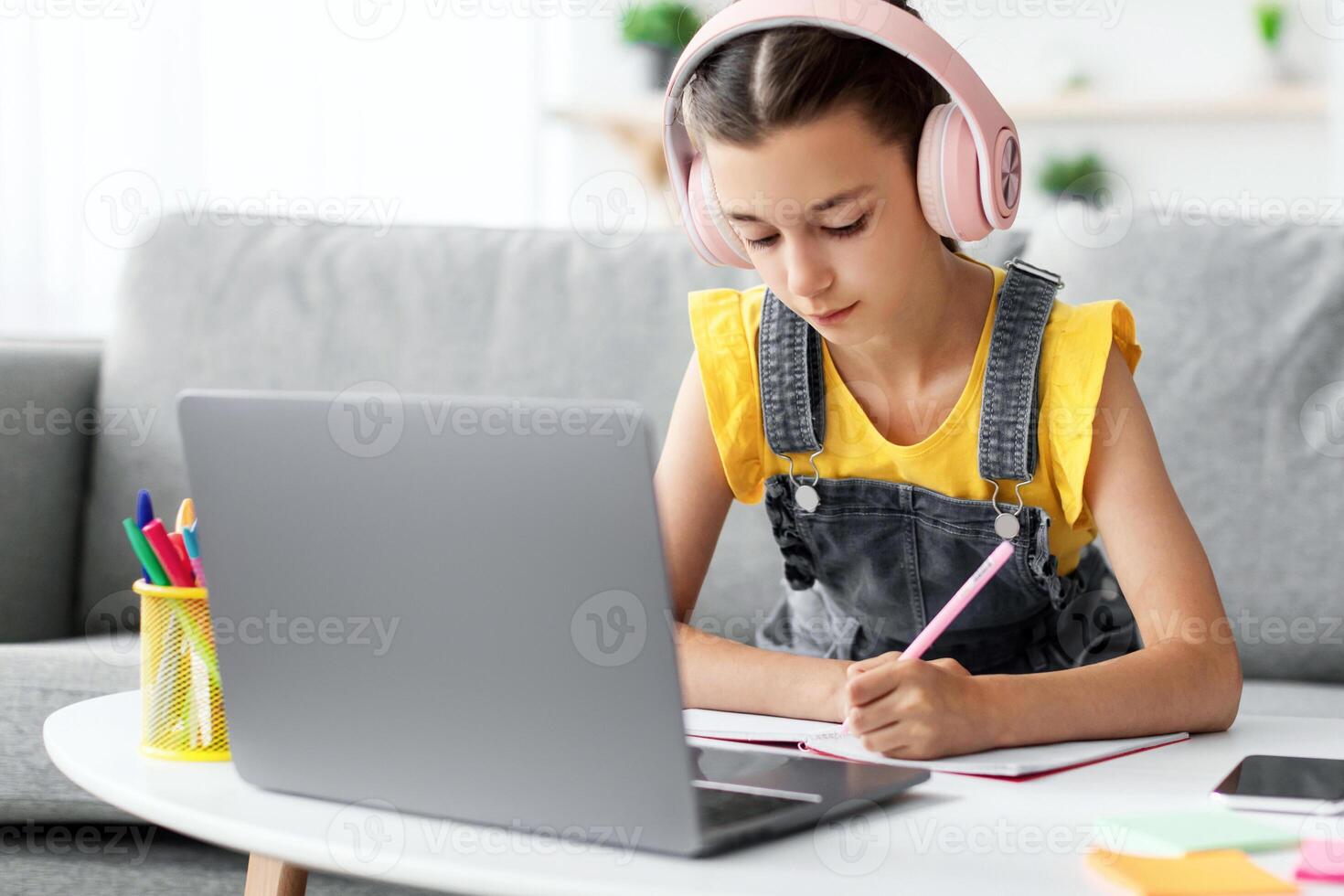 Doing Homework. Portrait of diligent teen girl in headphones studying remotely, using pc preparing for exam, schoolgirl learning online, watching webinar making notes. Distance education concept photo