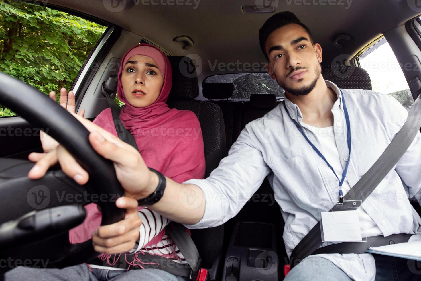 Nervous Muslim Lady In Hijab Having Driving Lesson With Instructor, Male Teacher Helping Islamic Female Student To Drive Car, Holding Steering Wheel, Closeup Shot Inside Of Automobile Vehicle photo